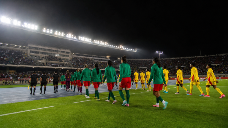 Women's national teams walk onto a floodlit football pitch