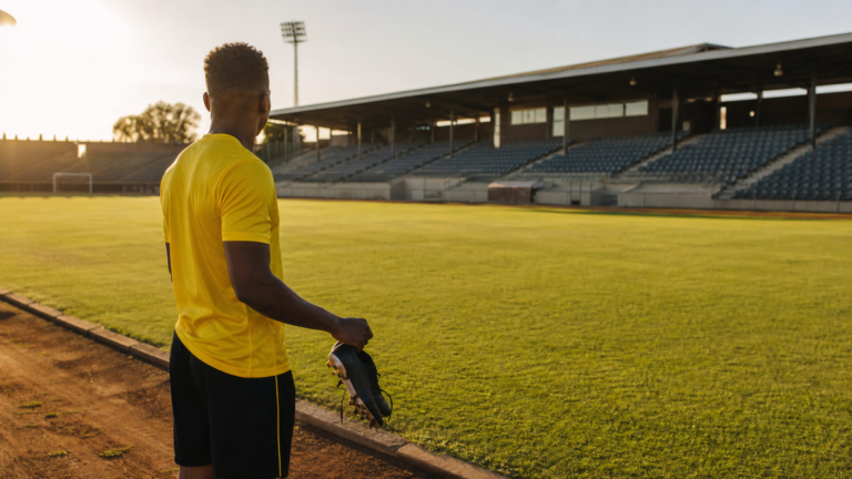 An anonymous footballer in a yellow training shirt looking across an empty pitch